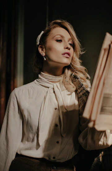 A woman in white shirt and pearls standing next to a mirror.
